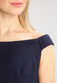 Dunkelblaues Kleid mit einem Wabenmuster. Verfügt über ein schulterfreies Design und eine elegante, taillierte Silhouette.