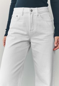 Biele rifle s širokými nohavicami z denimu s vysokým pásom, obsahujúce bočné vrecká, zapínanie na gombík a hladkú textúru.