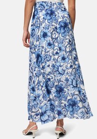 Jupe maxi avec un motif floral bleu sur fond blanc, fabriquée en tissu léger avec un design fluide et une taille élastique.
