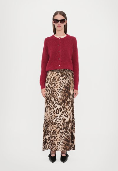 Cardigan rosso in lana con chiusura a bottoni, abbinato a una lunga gonna beige con stampa leopardata. La modella indossa occhiali da sole neri angulari e scarpe nere a punta.