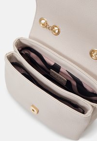 Beżowa skórzana torebka o fakturowanej powierzchni, z złotymi okuciami, dwiema wewnętrznymi przegrodami oraz wzorzystą podszewką w kolorach różowym i czarnym.