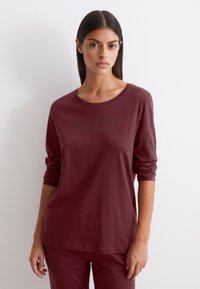 Camicia a maniche lunghe bordeaux con scollatura rotonda e maniche arrotolate. Presenta una stampa logo discreta sul petto. Tessuto morbido al tatto.