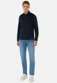 Marineblauwe longsleeve polo met kraag, met drie knopen bij de hals, gecombineerd met lichtblauwe jeans en witte sneakers.