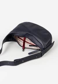 Borsa a tracolla in pelle blu navy con forma curva, chiusura con zip, fodera a motivo crema e dettaglio della tasca interna rossa.