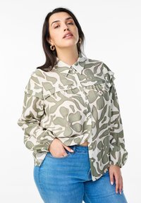 Button-up shirt in a light fabric, featuring an abstract green and white camouflage pattern, with a classic collar and chest pockets.