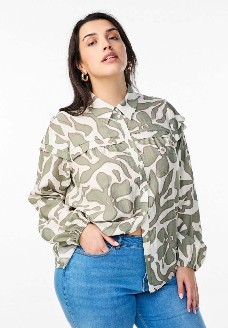 Button-up shirt in a light fabric, featuring an abstract green and white camouflage pattern, with a classic collar and chest pockets.