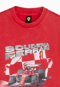 Camiseta de algodón roja con un gran gráfico de un coche de carrera Ferrari y el texto "SCUDERIA FERRARI" en plateado metálico.