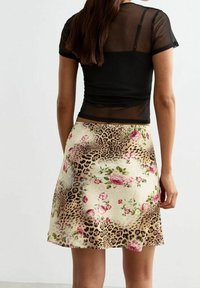 Top corto negro de manga corta y transparente, combinado con una falda acampanada con estampado de leopardo y detalles florales en rosa y verde sobre un fondo crema.