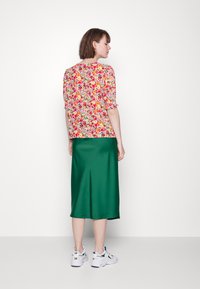 Top de flores de manga curta em vermelho, amarelo e verde; combinado com uma saia longa de cetim verde e ténis brancos com detalhes verdes.