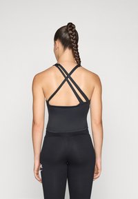 Svart athletic tank top med et tettsittende design, med kryssede stropper bak og paret med høyde liv svart leggings.