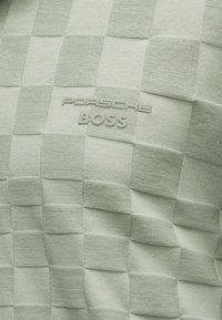 Πράσινο καρό υφασμάτινο με υφή και ανάγλυφα γράμματα "PORSCHE BOSS" σε τόνους πράσινου που ταιριάζουν.
