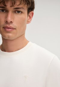 Witte sweatshirt met een ribbelkraag, voorzien van een subtiel geborduurd ontwerp op de linkerkant van de borst en een gladde, zachte textuur.