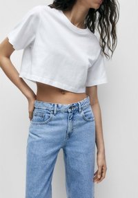 Witte cropped t-shirt met korte mouwen, gecombineerd met lichtblauwe high-waisted jeans met een knoopsluiting en vijf zakken.