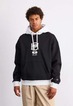 Sudadera negra con detalles en gris, que presenta un bolsillo frontal y un logo impreso. Hecha de algodón, tiene un ajuste holgado y capucha con cordón.