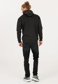 Kolgrå hoodie med stor huva och ribbade ärmslut, kombinerad med svarta jeans. Modell som bär grå sneakers med flerfärgade detaljer.