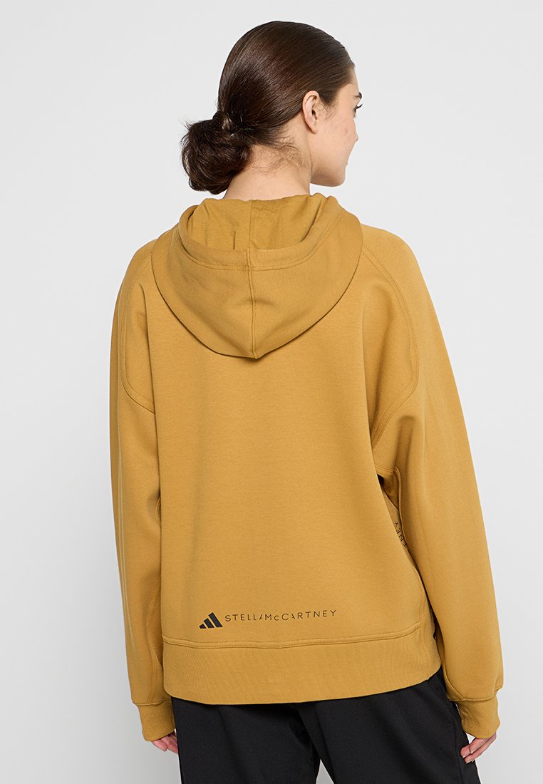 Sudadera con capucha de color mostaza amarilla y corte relajado. Presenta un logo en la parte posterior y un ribete acanalado. Fabricada con un tejido suave y texturizado.