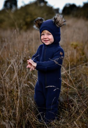 Navy blue fleece onesie with a zip front, featuring a hood and faux fur ear accents, worn by a child in tall grass.