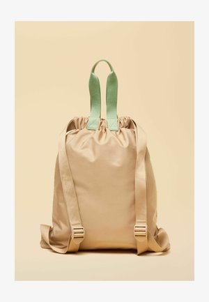 Beiger Rucksack mit Kordelzug, breiten mintgrünen Tragegriffen und verstellbaren beigen Schultergurten vor hellem Hintergrund.