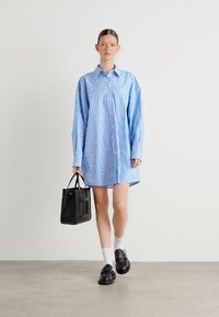 Modra in bela črtasta oversize srajčna obleka z gumbi, dolgimi rokavi, nošena z črno torbico, belimi nogavicami in črnimi čevlji.