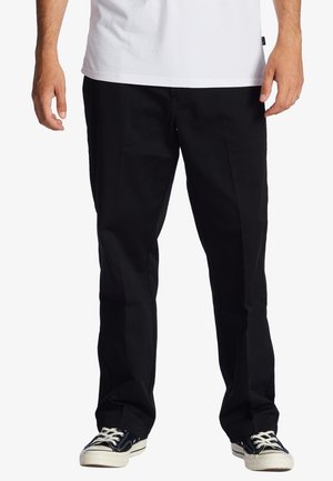 Black cotton twill pants with a straight fit, featuring front pockets and a smooth, flat waistband. Completed with black and white sneakers.