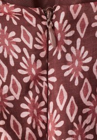 Zbliżenie na mauve tkaninę z jasnoróżowymi kwiatowymi i diamentowymi wzorami oraz zamkniętym zamkiem błyskawicznym na środku.