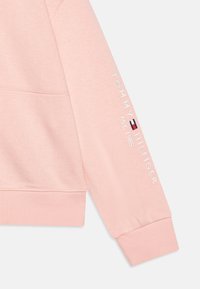 Růžová mikina s žebrovanými manžetami a lemem. Na rukávu je bílý text "TOMMY HILFIGER" a "EST. 1985" spolu s malým logem.