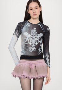 Long-sleeve black and blue top with intricate graphic designs, paired with a pink frayed skirt featuring an elastic waistband.