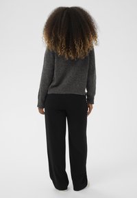 Pilkas megztinis ir juodos plačios keln�ės. Minkšta tekstūra, laisvas siluetas, ir nusidėvėjęs megztinio kraštas. Dominuoja neutralios spalvos.