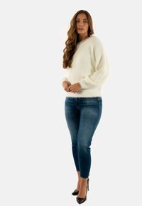 Maglione bianco soffice con scollatura tonda e maniche a palloncino, abbinato a jeans skinny in denim scuro e tacchi alti neri.