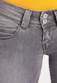 Vaqueros grises con un diseño ajustado, dos botones metálicos en la cintura y un ligero desgaste; tejido de denim liso de peso medio.