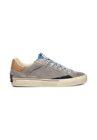 Sneaker in suede grigia con un accento blu scuro, suola in gomma chiara e dettagli neri. Presenta lacci grigi e blu e un tab in pelle marrone sul tallone.
