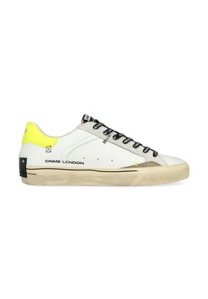 Basket en cuir blanc avec lacets noirs, accents gris et contrefort de talon jaune vif. Présente une semelle en caoutchouc plate et une marque sur le côté.