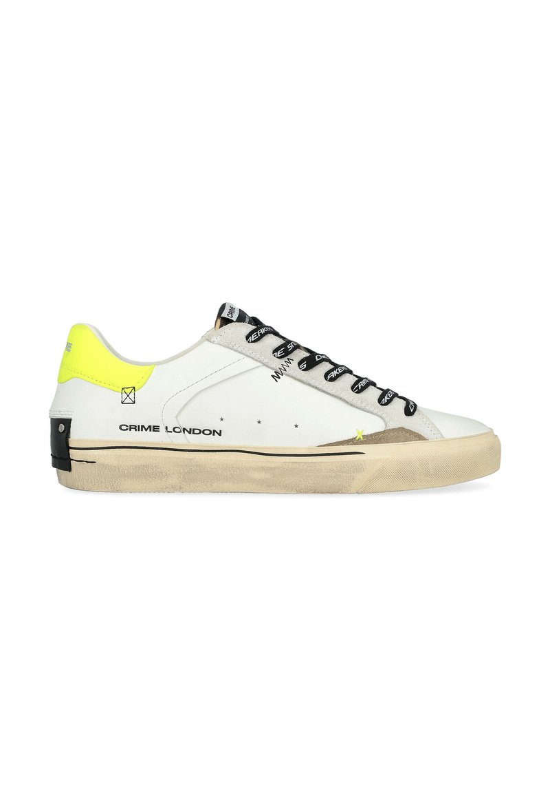 Sneaker in pelle bianca con lacci neri, accenti grigi e un tallone giallo brillante. Presenta una suola in gomma piatta e il branding sul lato.