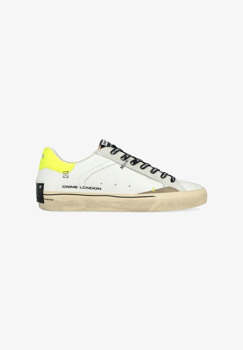 Sneaker in pelle bianca con lacci neri, accenti grigi e un tallone giallo brillante. Presenta una suola in gomma piatta e il branding sul lato.