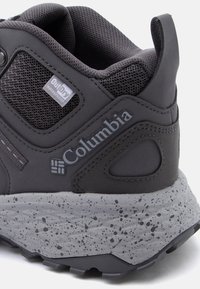 Κοντινό πλάνο της φτέρνας ενός μαύρου υποδήματος πεζοπορίας Columbia με γκρι πουα σόλα, υφασμάτινο πλέγμα και ετικέτα αδιαβροχοποίησης OutDry.