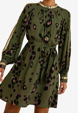 Olivengrøn kjole med sorte og lilla leopardpletter, guld palietkant på krave, ærmer og manchetter, med lange ærmer og taljebånd.