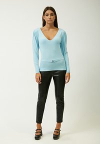 Maglione aderente azzurro chiaro con scollatura a V profonda, texture a costine e maniche lunghe. Abbinato a pantaloni skinny in finta pelle nera e tacchi.