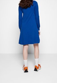 Blå klänning med lång ärm, knä-lång fåll och avslappnad passform. Med vita strumpor och sneakers i orangea accenter med svarta sulor.