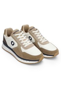 Adidași crem și albi cu șireturi, cu accente din suede maro, logo circular negru pe laterale și interior căptușit crem.