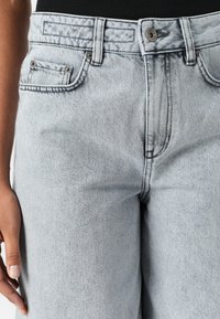 Ljust grå denimjeans med hög midja, rak passform, framfickor och metallknappsstängning. Utmärkande slitningar och sömdetaljer.