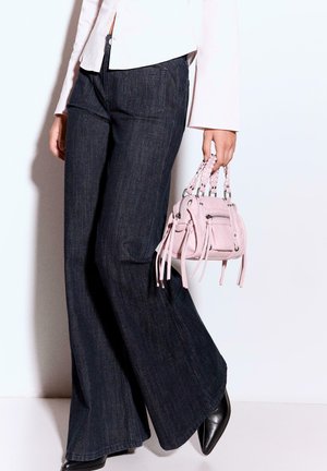 Rosa Lederhandtasche mit geflochtenen Griffen, silberner Hardware und Fransenakzenten. Kombiniert mit weit geschnittenen, dunklen Denim-Jeans und spitzen schwarzen Absatzschuhen.