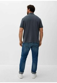 Donkergrijze polo met een kraag, gedragen met een blauwe jeans en witte sneakers. Zichtbare stiksels en details van de achternaad.