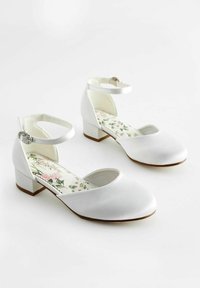 Pantofi din satin alb, cu curea la gleznă și toc mic. Interiorul are un model floral. Design cu vârf rotund și accente hardware minimaliste.