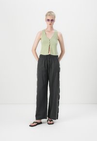 Green cropped top with a V-neck and button closure, paired with black wide-leg pants featuring decorative side trim and sandals.