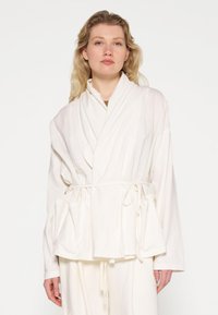 Witte, langwerpige omslagjas met een ceintuur om de taille, gegoten kraag en zijzakken. Zachte stof met een gladde textuur.