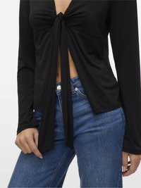 Fekete hosszú ujjú felső, elöl megkötve, amely megmutatja a hasat, magas derekú kék farmernadrággal párosítva egy személyen.