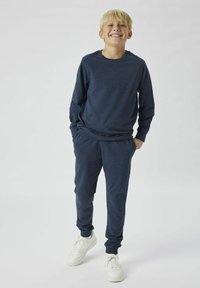 Chemise à manches longues bleu marine assortie avec un pantalon de jogging, tous deux en tissu doux. Les détails des chaussures incluent des baskets blanches à lacets.