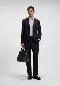 Black suit jacket with textured pattern, white shirt featuring small dots, black trousers, and a black leather bag. Black dress shoes.