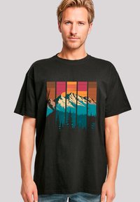 Zwarte t-shirt met een kleurrijke afbeelding van bergen en een bos in teal, oranje en roze. Korte mouwen en een losse pasvorm.