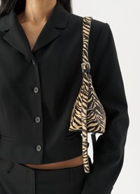 Zebra-patterned handbag made of textured fabric, featuring a triangular shape and a black strap, paired with a black blazer.